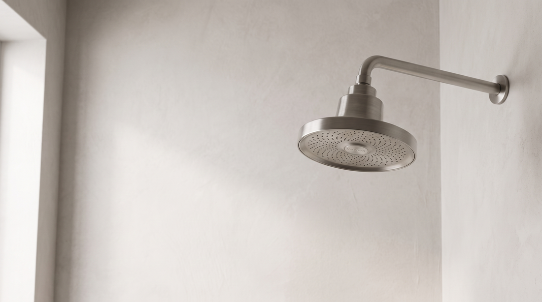The showerhead installed on a shower arm in a plaster-walled bathroom.